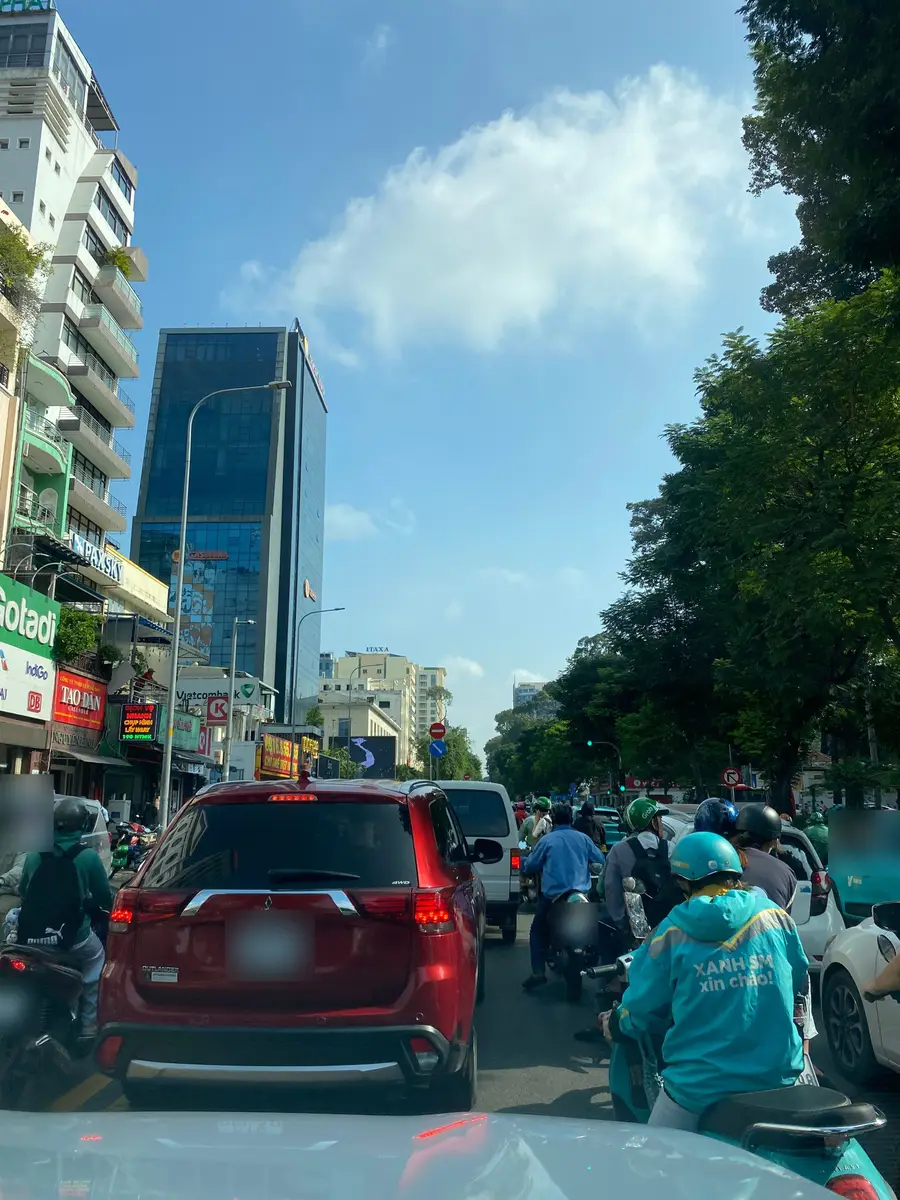 Dense morning traffic in central Ho Chi Minh City: motorbikes and an SUV waiting at a junction between office towers