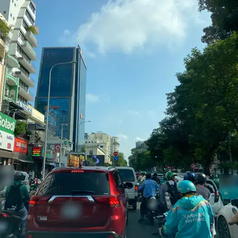 Dense morning traffic in central Ho Chi Minh City: motorbikes and an SUV waiting at a junction between office towers