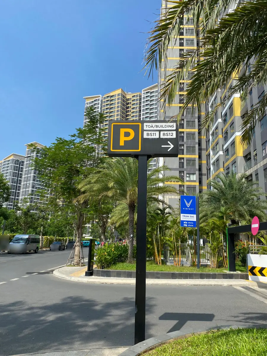 Bilingual parking sign reading 'Toà/Building BS11 BS12' with an EV charging station sign, in front of high-rise apartments