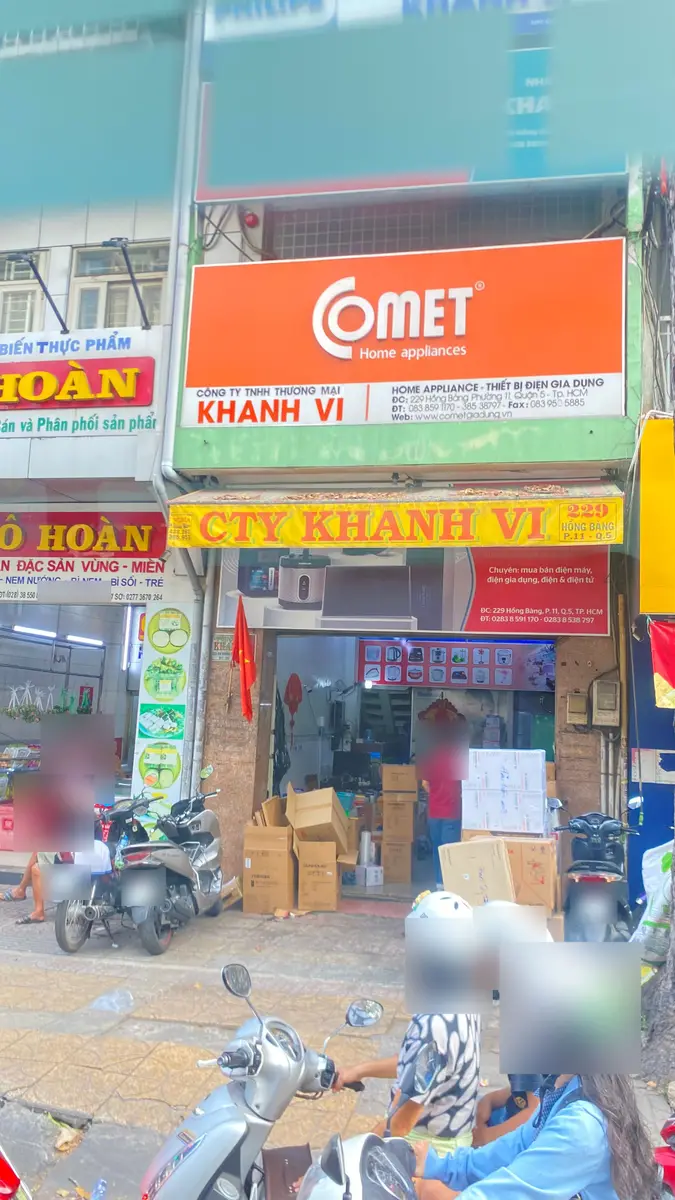 Shopfront of a home-appliance company with dense Vietnamese signage, neighbouring food shop signs and motorbikes on the pavement