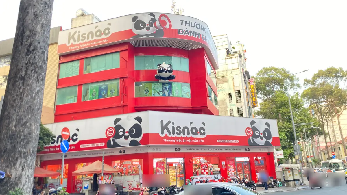 Corner snack store with large red and white Vietnamese signs, slogans and a hotline number, with street traffic below