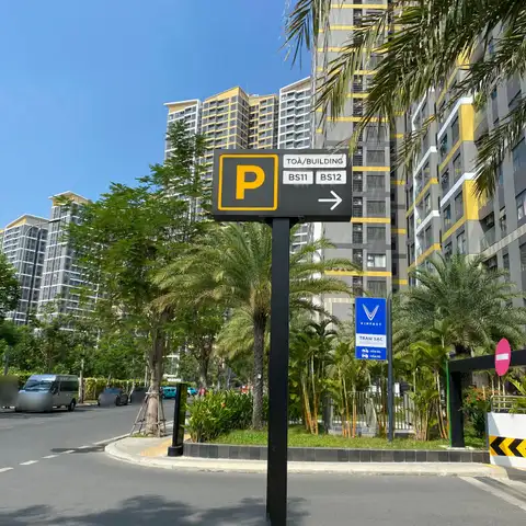 Bilingual parking sign reading 'Toà/Building BS11 BS12' with an EV charging station sign, in front of high-rise apartments