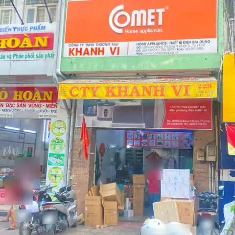 Shopfront of a home-appliance company with dense Vietnamese signage, neighbouring food shop signs and motorbikes on the pavement