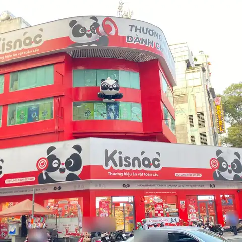 Corner snack store with large red and white Vietnamese signs, slogans and a hotline number, with street traffic below